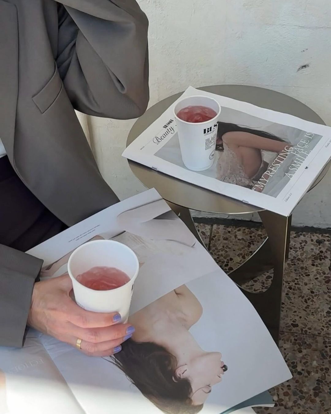 Person holding a cup with a magazine open on a table